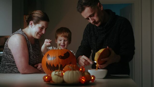 Happy family making jack o lantern by carving pumpkins. Halloween celebration.