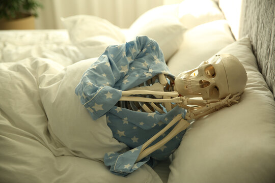 Human skeleton in pajamas lying on bed indoors