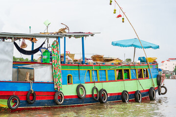 A large colourful boat on a river with an umbrella and tires strung from the sides