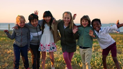 Children group, diversity embrace and smile in park, wave hands and summer by ocean on school trip. Happy multicultural kids, waving and solidarity by sea on lawn for unity, equality or young friends - Powered by Adobe