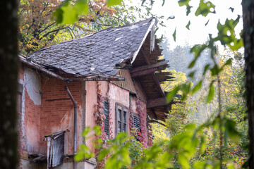 An old house ruin with a derelict roof, seen from between trees