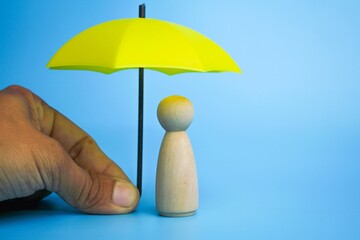 Hand holding yellow umbrella with girl peg doll on blue background. The concept of insurance...