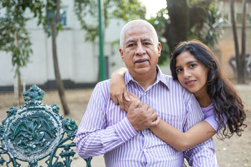 Portrait of grandfather and granddaughter sitting in a bench.