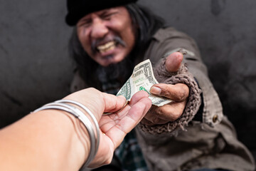 Selective focus of hand kind person giving one dollar bill money to old man homeless. Asian beggar...