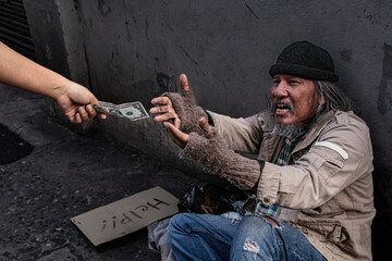 Selective focus of Asian homeless man feel happy and crying receives one dollar bill money from a...