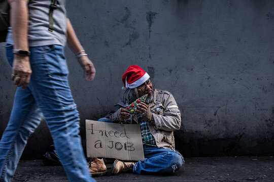 Asian homeless man wearing christmas hat sitting on side of road holding a toy christmas tree and sign asking for help, need a job. old man madman on home on money. Poverty and social issue concept.