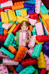 Fototapeta na wymiar Little smiling girl playing with colorful big blocks in playroom. Toys and games in nursery room. Leisure and recreation. Happy baby girl a birthday party. Entertainment center for children. Top view.