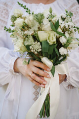 Bride holds a wedding bouquet of flowers in her hands in embroidered dress. Ethnic wedding in national costumes. Ukrainian style, beautiful girl in national clothes outdoor.