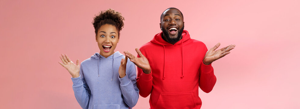 Guys Receive Nice Surprise. Two Attractive Carefree Surprised Happy African Man Woman Clapping Hands Joyfully Greeting Welcoming Guests Inviting People Joing Party Standing Friendly Pink Background