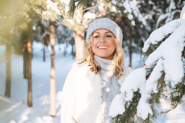 Happy blonde woman in winter clothes hands near face in snowy winter forest