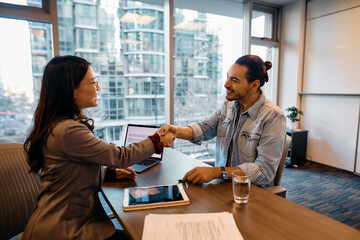 Happy Hispanic job candidate shaking hands with Asian businesswoman after successful interview in office.