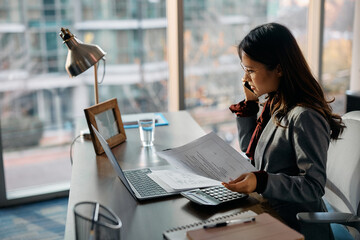 Asian businesswoman talking on cell phone while working in office.