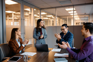 Asian female executive getting applause from colleagues after successful business meeting in office.