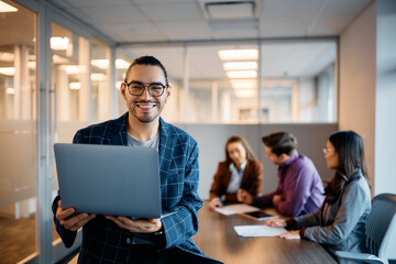 Happy Hispanic businessman using laptop during meeting with coworkers in office.