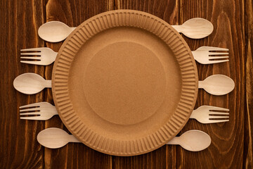 Wooden forks and spoons and paper plate on wooden background