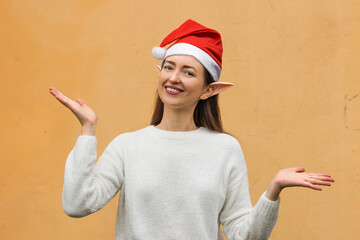 Smiling young woman with elf ears in red santa hat. Yellow background. Happy Santa's helper on...
