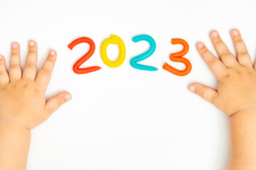 A little child's hands playing with figurine 2023 of plasticine on white background. New Year 2023. Merry christmas concept