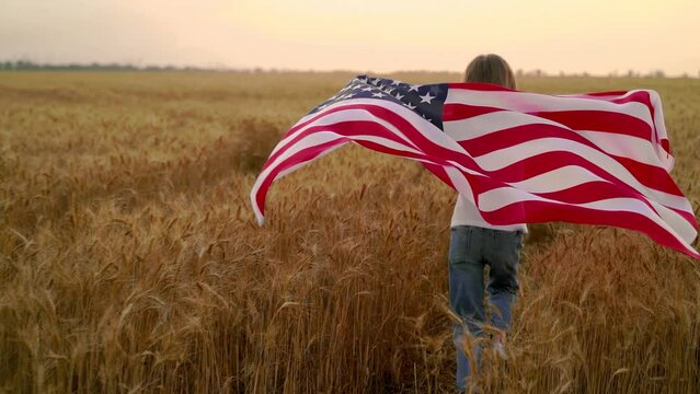 Back view of patriotic girl with USA flag which runs on a wheat field. 4k. Slow motion 