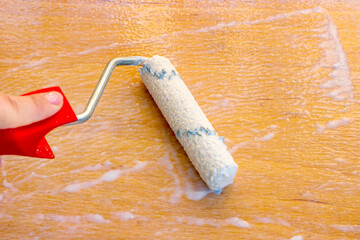 Paint roller with white acrylic varnish for wood lacquering the wooden plank during the interior renovation in home.