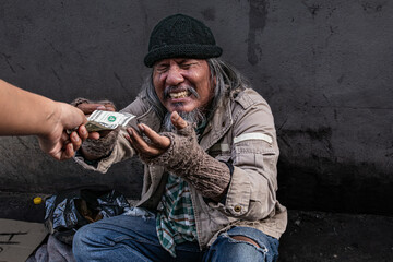 Selective focus of Asian homeless man feel happy and crying receives one dollar bill money from a...