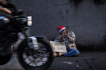 Asian homeless man wearing christmas hat sitting on side of road holding a toy christmas tree and...