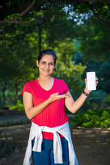 Happy Indian Runner woman showing smartphone screen at park.