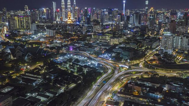 Aerial time lapse overlooking a busy roundabout and city streets against a city skyline in the background at night with city lights in Kuala Lumpur, Malaysia. Tilt up motion time lapse. Prores 4KUHD