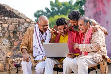 Indian villagers setting at in front of home and using laptop.