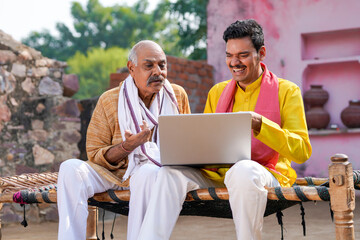 Young indian farmer showing some detail to his father in laptop.