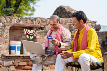 Young indian farmer using laptop and card with his father at his home