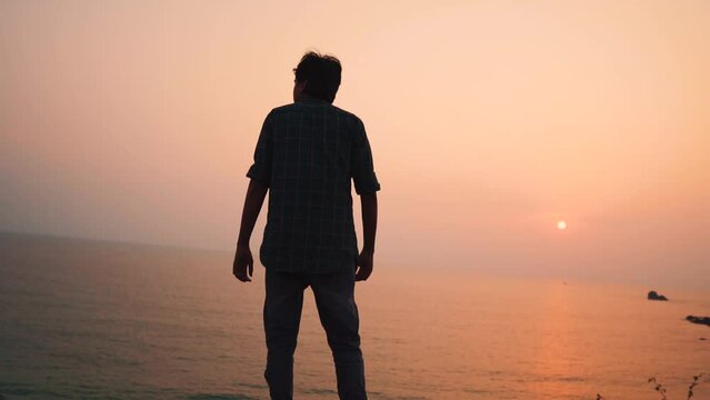 Indian man looking at the sea during the sunset at top of the hill besides Cabo De Rama beach in Goa, India. Man looking at the sun setting on the sea. Natural background. Man enjoying sunset.	