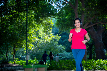 young indian woman with earphones listening music during jogging at park.