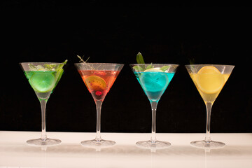 Quatre verres de différents cocktail avec des cocktails colorés sur un fond noir.