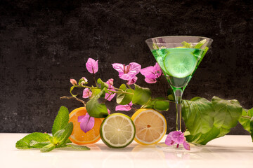 Verre à cocktail de couleur vert avec des fruits sur fond noir.