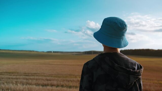 teen alone boy in the field looking into the distance in summer day, back view