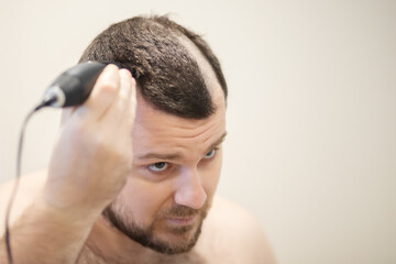 a man cuts his head with a clipper, self-shaving his head baldly