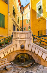 Fototapeta na wymiar Symbolic stone stairs and fountain at Rue du Poilu street and Place du Conseil square in old town of Villefranche-sur-Mer resort town in France