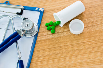 Medical clipboard with stethoscope and pills on desk