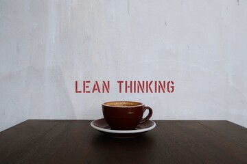 Coffee cup on copy space white wall with text LEAN THINKING, concept o  the way of  thinking about...