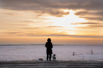 Silhouette of a man and a dog against the background of a winter field at sunset. The concept of a single person. - 552772404