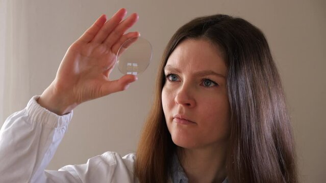 optometrist woman is holding and looking at an eyewear glass lens for quality control Lens manufacturing