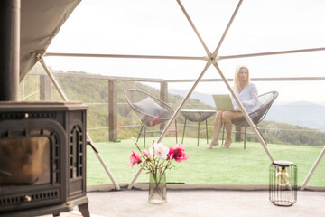 Hipster girl working with a laptop at home office in a glamping in the mountains with great views.