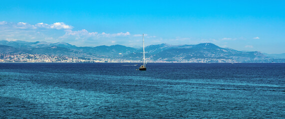 Panoramic view of harbor and yachts with French riviera shore in background seen from Azure Cost of Mediterranean Sea in Antibes resort town in France