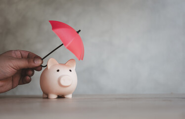 Finance insurance and safe investment concept. Hand hold small red umbrella over piggy bank protect...