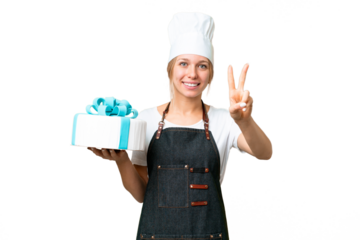 Young pastry blonde woman with a big cake over isolated chroma key background smiling and showing victory sign