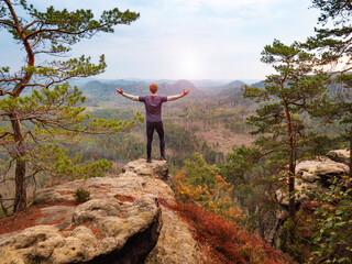 Happy man with raised arms is shouting to valley bellow  from sharp rocky edge