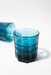 Two beautiful blue glass glasses for drinks and alcohol on a white background. One glass is in the foreground, one glass is in the background