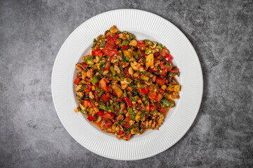 Gavurdagi salad on dark background. Turkish cuisine appetizer flavors. Salad made with walnuts, tomatoes, green peppers, onions, parsley and cucumbers. Top view. close up