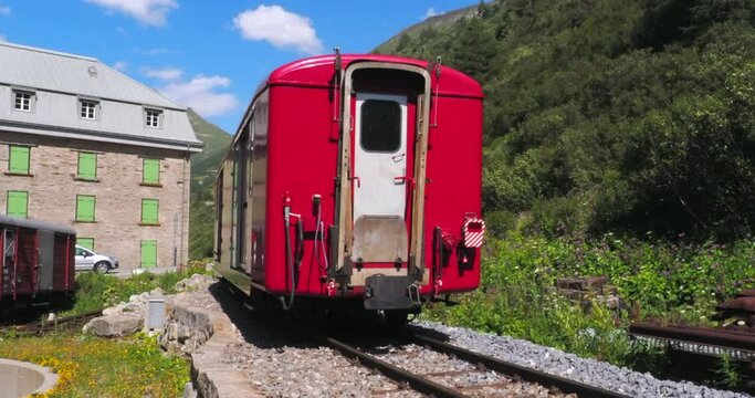 Gletsch, Switzerland - July 15, 2022: A red train of Furka railway leaving the station of Gletsch under the Rhone Glacier