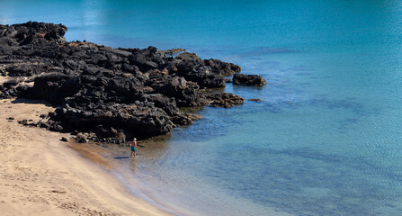 Aerial view of an unrecognizable senior man bathing alone in Lanzarote. Crystal clear turquoise water. Beautiful beige sandy empty beach with dark volcanic stones. Costa Teguise, Canary Islands, Spain